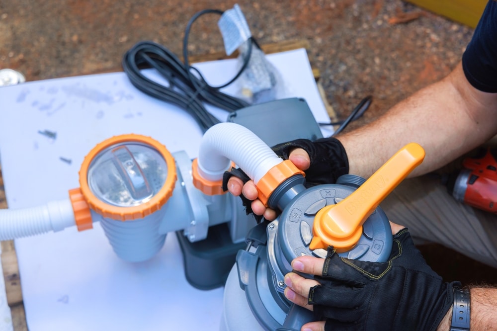 Pompe de filtration Bestway : Raccorder le tuyau du filtre. Montage de la pompe de filtration Bestway. Des mains gantées raccordent le tuyau flexible à la vanne multivoies orange.